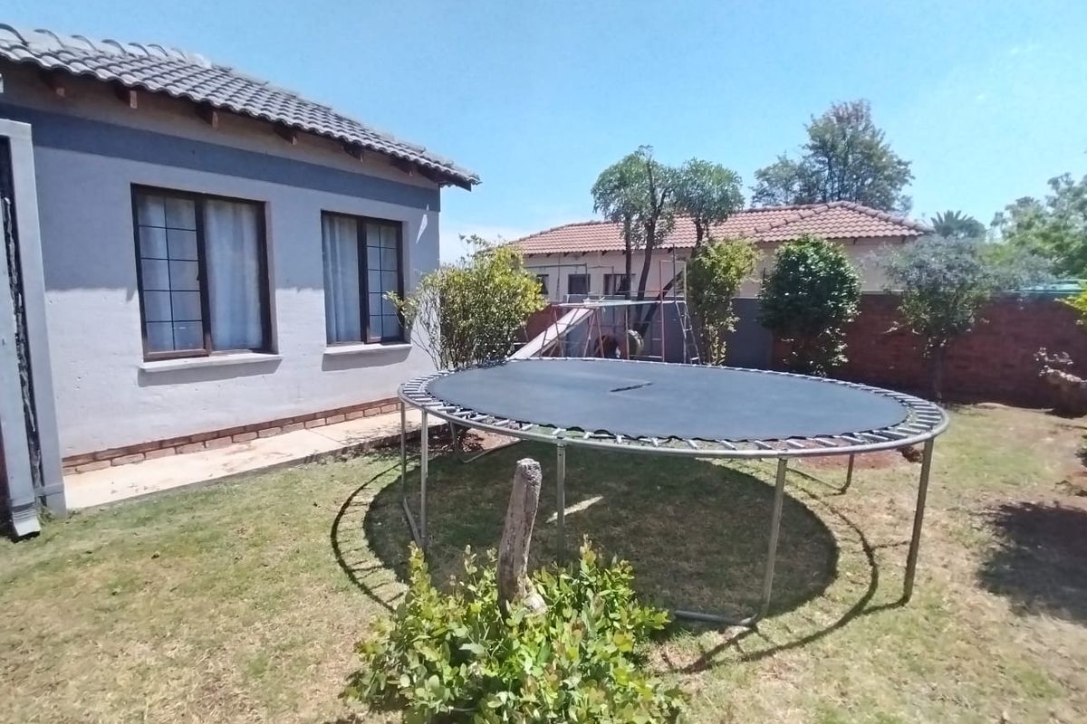 Rear garden area featuring a lawn, established trees, and a brick boundary wall, adjacent to the main house structure.