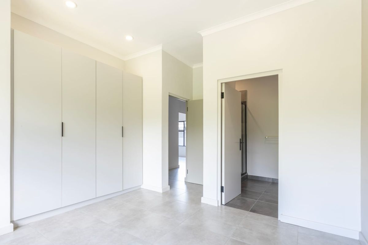 A bright bedroom featuring built-in floor-to-ceiling cabinetry, neutral tiled flooring, recessed lighting, and direct access to an en-suite bathroom.
