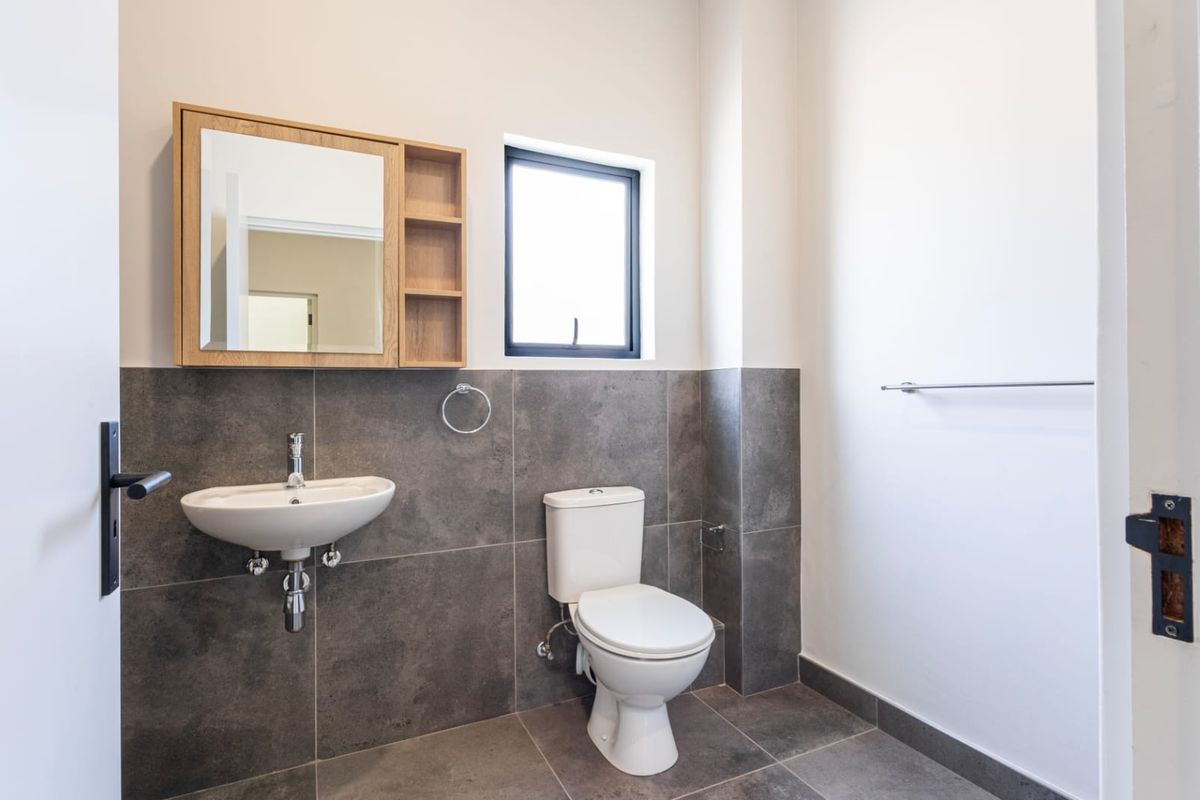 A modern bathroom featuring a wall-mounted basin, a close-coupled toilet, and a wooden medicine cabinet, finished with dark grey floor-to-ceiling wall tiles.