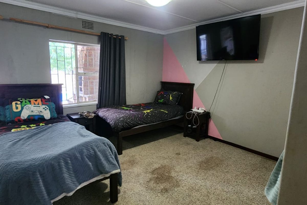 A bedroom featuring two single beds, large windows with security bars, and neutral wall finishes with a decorative painted accent.
