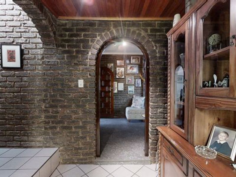 A characterful hallway featuring exposed brick walls, arched architectural transitions, a warm timber ceiling, and tiled flooring leading into an adjacent living space.