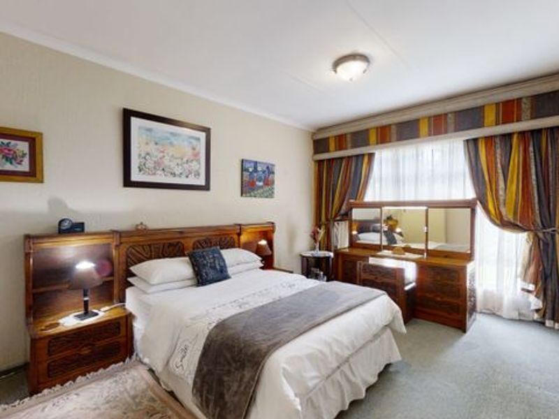 A bedroom featuring a built-in wooden headboard and matching vanity unit, with carpeted flooring and window treatments.