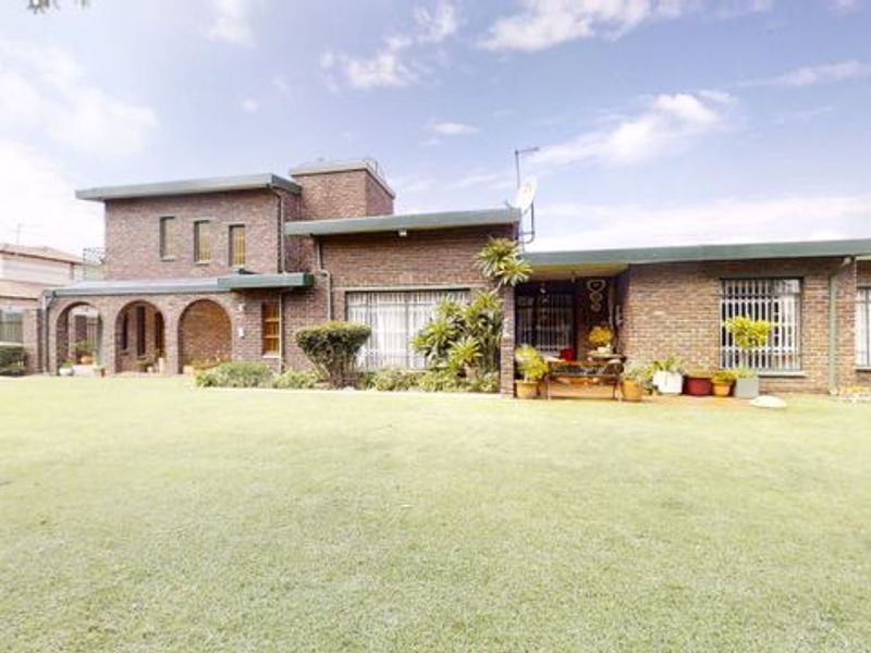 A rear view of a face brick house featuring an arched covered patio, security bars on windows, and a spacious lawn area.
