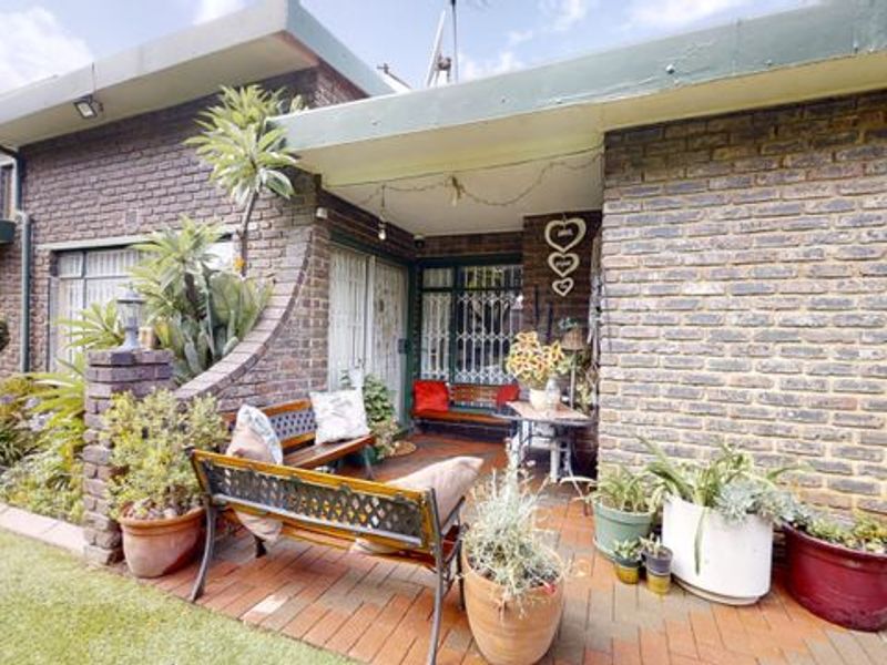 A covered brick patio area featuring paved flooring and security fixtures, providing a sheltered outdoor space adjacent to the main house structure.