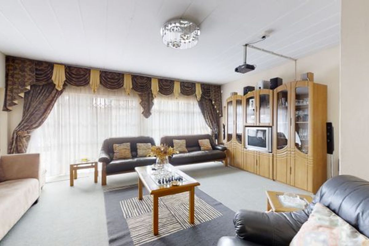 Spacious living room featuring large windows, a ceiling-mounted projector, and neutral carpeting, offering a comfortable area for relaxation and entertainment.