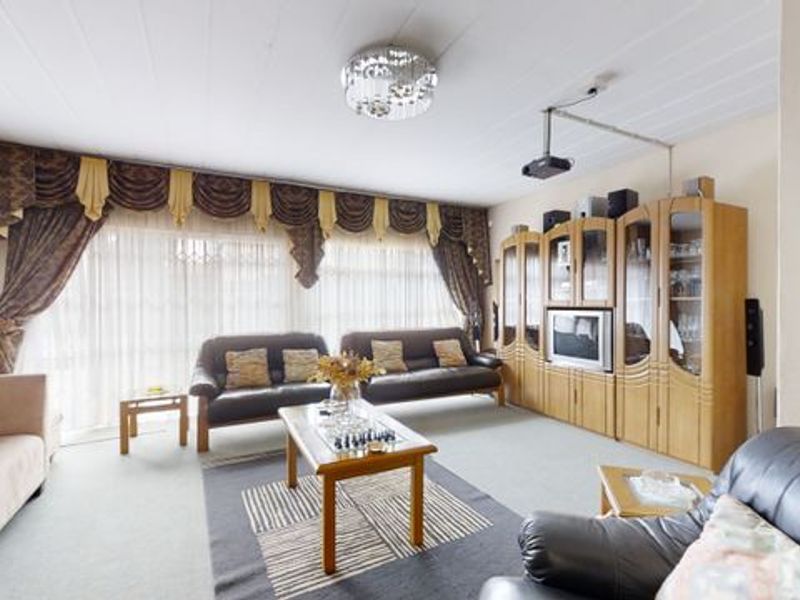 Spacious living room featuring large windows, a ceiling-mounted projector, and neutral carpeting, offering a comfortable area for relaxation and entertainment.