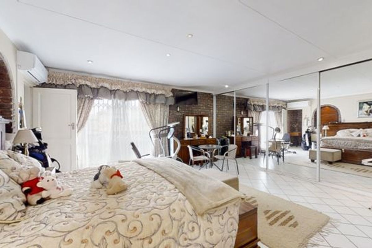 Spacious bedroom featuring tiled flooring, an exposed brick feature wall, built-in mirrored wardrobes, and an integrated air conditioning unit.