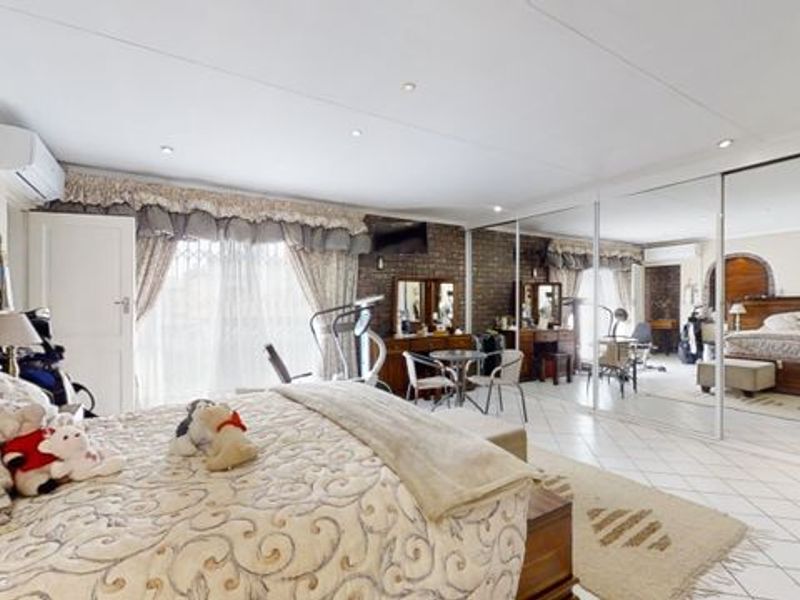 Spacious bedroom featuring tiled flooring, an exposed brick feature wall, built-in mirrored wardrobes, and an integrated air conditioning unit.