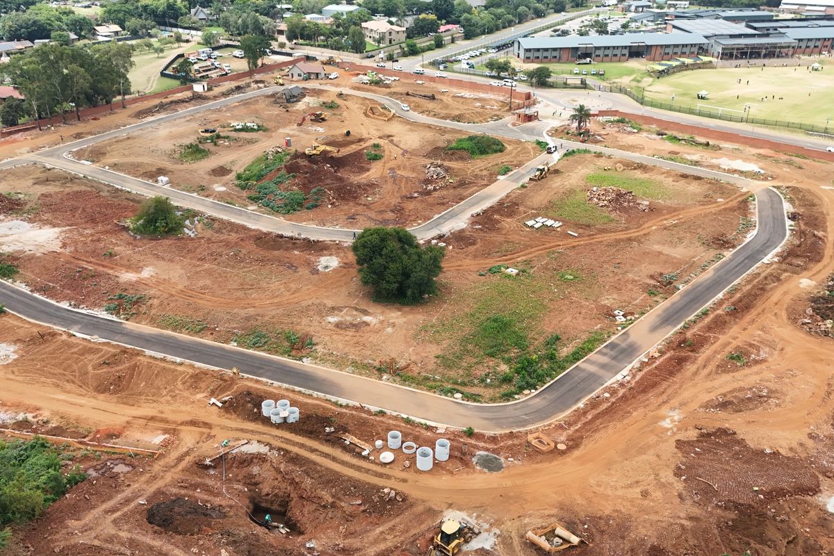 Aerial view of a residential development site showing cleared land, newly laid asphalt roads, and installed drainage infrastructure.