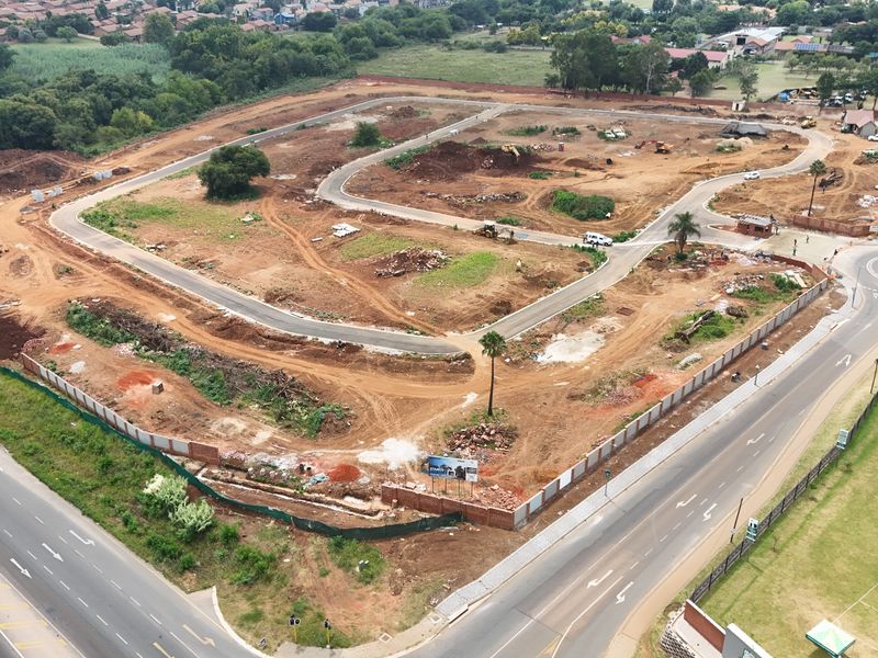 Aerial view of a residential development site showing cleared land, internal road infrastructure, and perimeter boundary walls under construction.