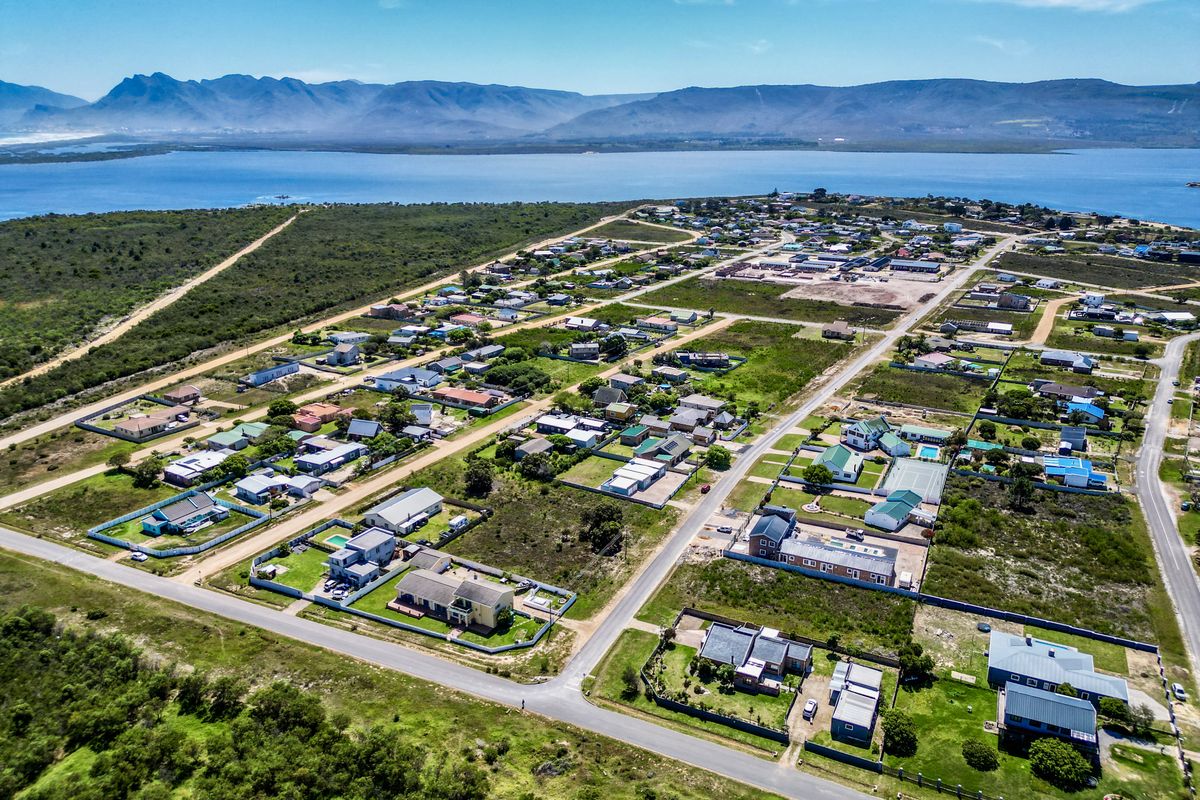 An aerial view of a coastal residential neighborhood featuring established housing plots, paved streets, and proximity to the lagoon and mountain range.