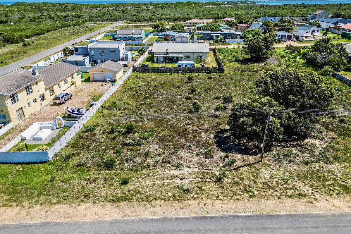 Aerial view of a vacant residential plot featuring natural vegetation, boundary fencing, and access to local infrastructure in a coastal neighborhood.