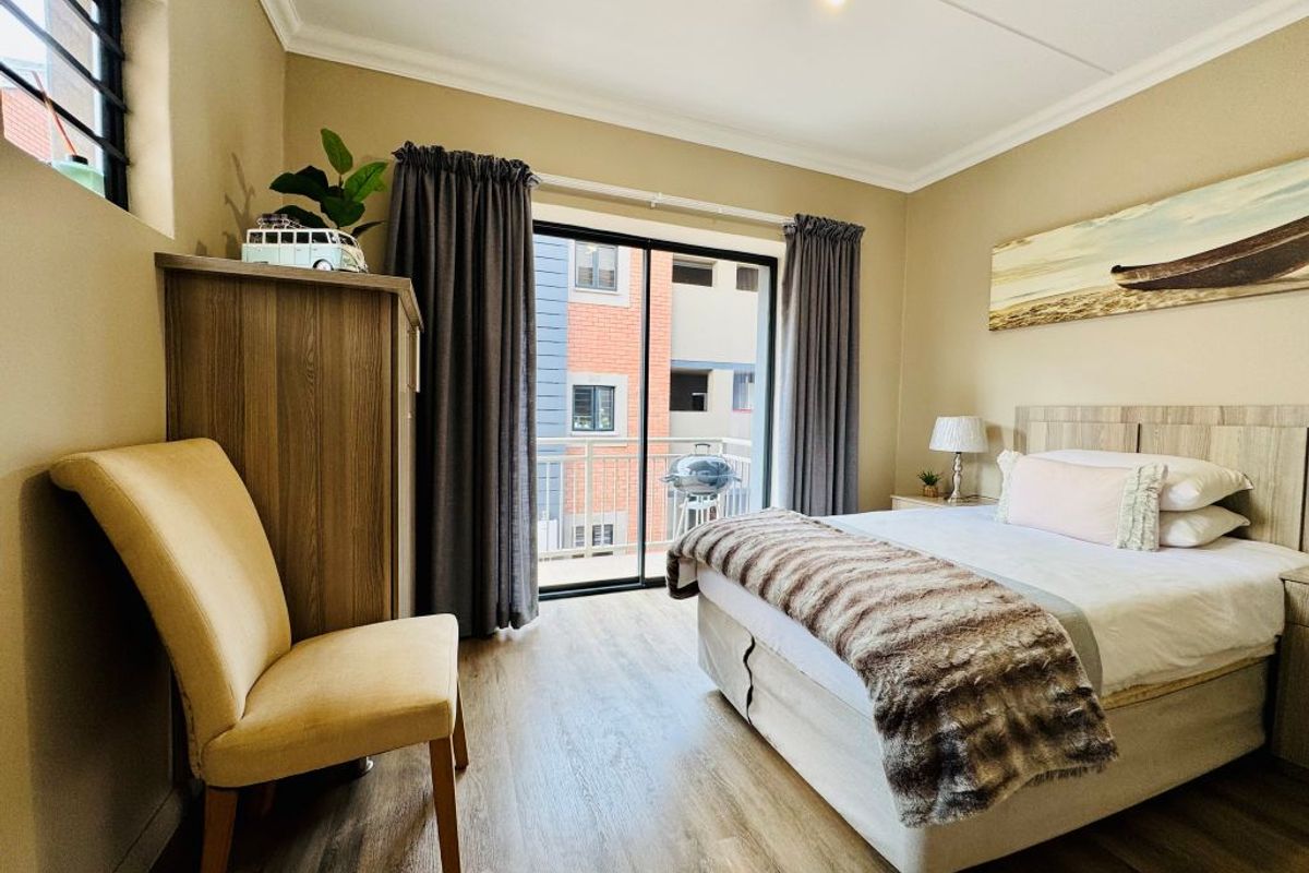 A well-maintained bedroom featuring wood-look flooring, built-in headboard, and sliding glass doors leading to a private balcony.