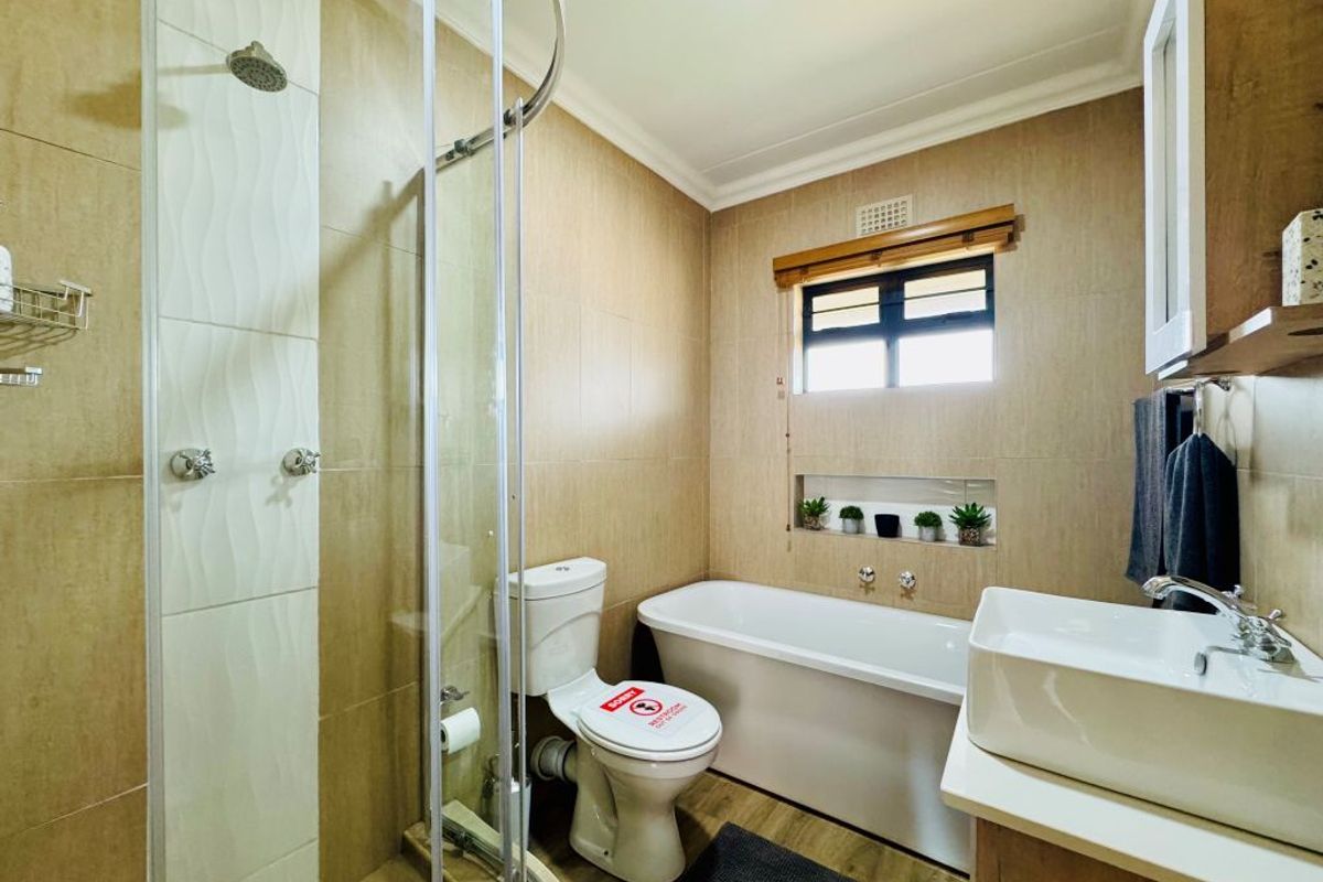 Modern bathroom featuring a glass-enclosed shower, a freestanding bathtub, a wall-mounted vanity with a vessel sink, and neutral wall tiling.
