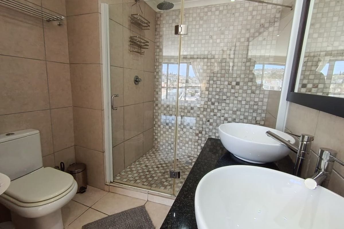 Modern bathroom featuring a glass-enclosed walk-in shower with mosaic tiling, dual vessel sinks on a granite vanity, and a standard toilet.