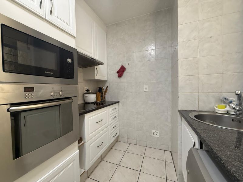 A compact kitchen featuring white cabinetry, granite countertops, a built-in oven and microwave, and tiled finishes throughout.