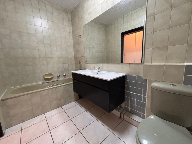 A functional bathroom featuring a built-in bathtub, a modern wall-mounted vanity with an integrated sink, and neutral ceramic tiling throughout.