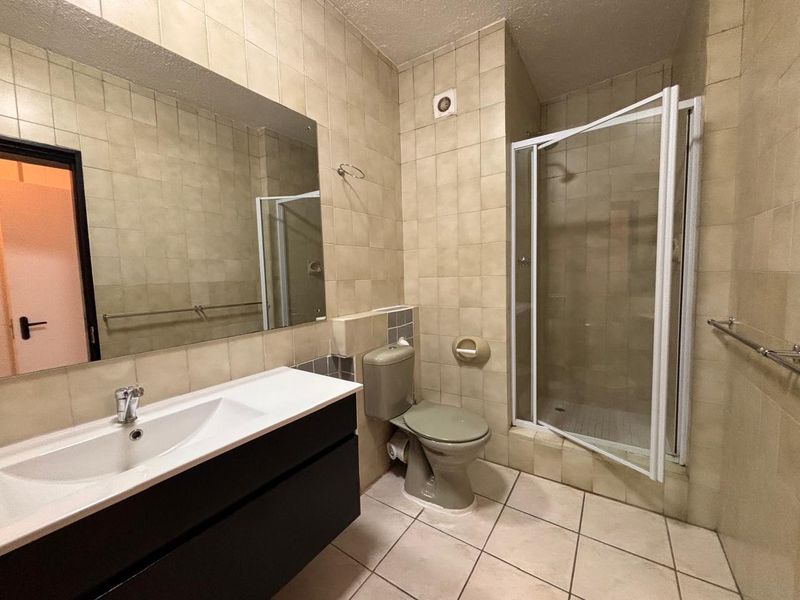 A functional bathroom featuring a vanity with integrated basin, a separate shower enclosure, and a toilet, finished with neutral wall and floor tiling.