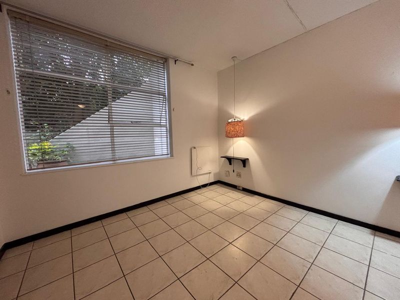 An empty bedroom featuring tiled flooring, a wall-mounted heater, and large windows with venetian blinds, offering a blank canvas for potential renovation.