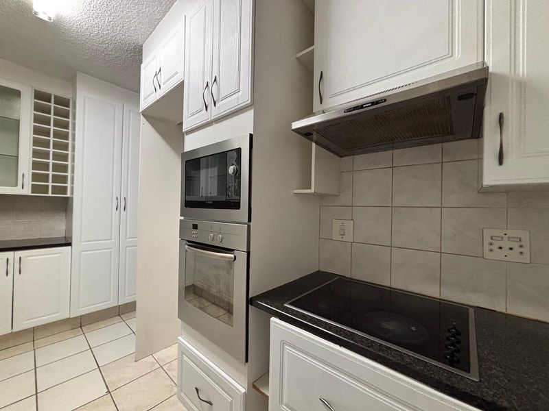 A functional kitchen featuring built-in appliances, granite countertops, tiled backsplash, and ample white cabinetry, offering a clean and practical workspace.