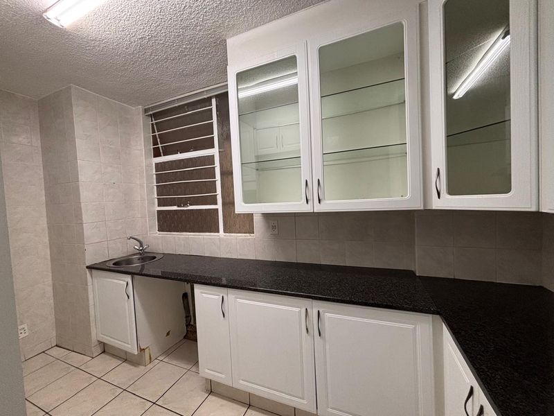 A functional kitchen featuring granite countertops, white cabinetry with glass-front uppers, tiled backsplash, and ceramic flooring, offering a clean canvas for potential updates.