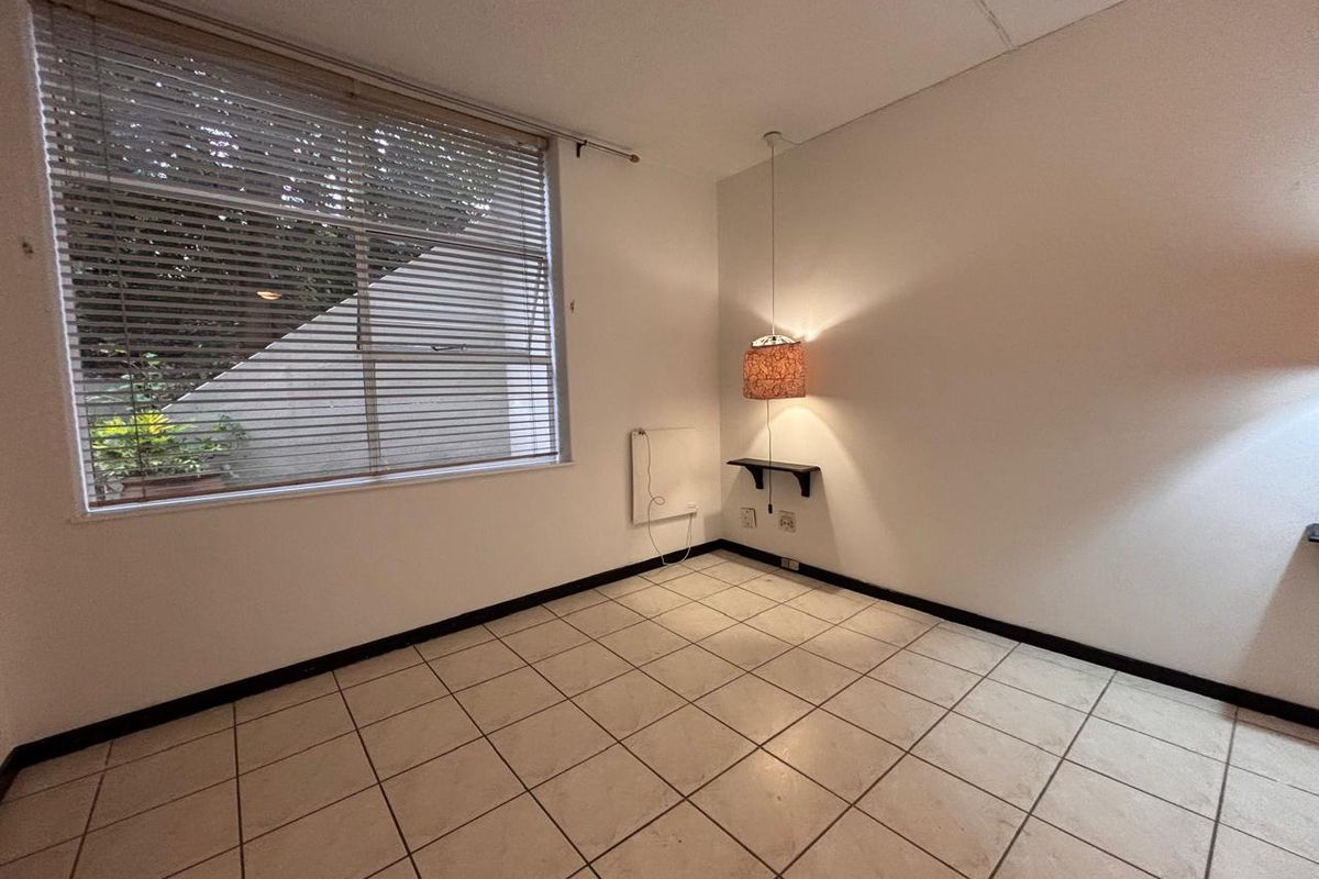 An empty bedroom featuring tiled flooring, a wall-mounted heater, and large windows with venetian blinds, offering a blank canvas for potential renovation.
