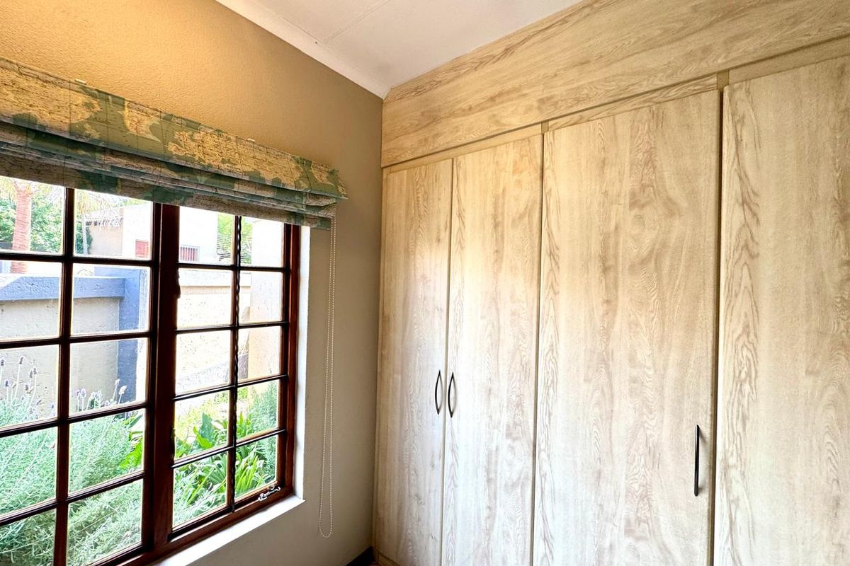 A bedroom featuring light wood-grain built-in cupboards and a window with a view of the garden.
