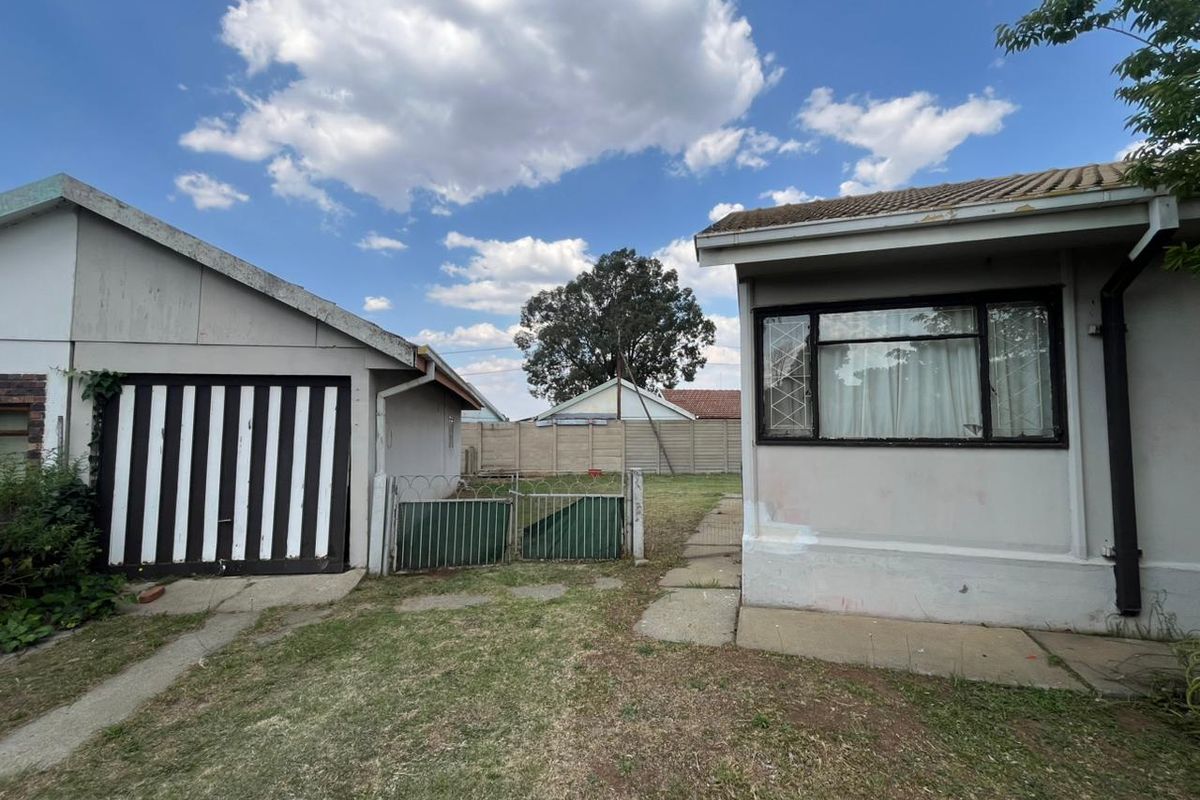 Rear view of the property showing a detached garage, concrete paving, and perimeter walling with security fencing.