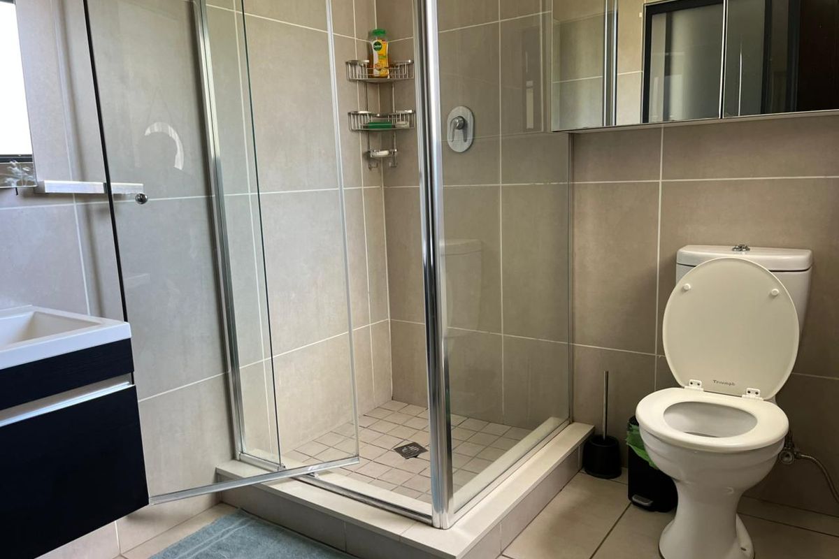 A modern bathroom featuring a glass-enclosed shower, a wall-mounted vanity, and a standard toilet with neutral floor-to-ceiling tiling.