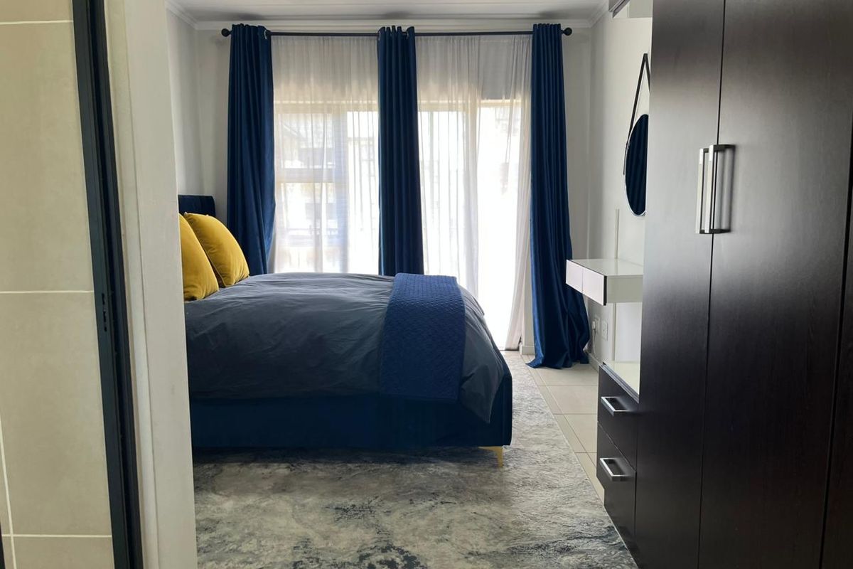 A well-maintained bedroom featuring built-in dark wood cabinetry and large windows with floor-to-ceiling curtains, providing ample natural light.