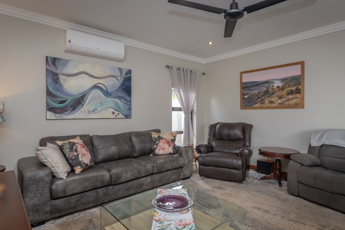 A well-maintained living room featuring crown molding, a ceiling fan, and a wall-mounted split-system air conditioner.