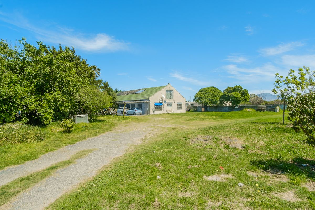 A wide-angle view of the rear exterior of the property, featuring a gravel driveway, expansive lawn, and a pitched roof structure.