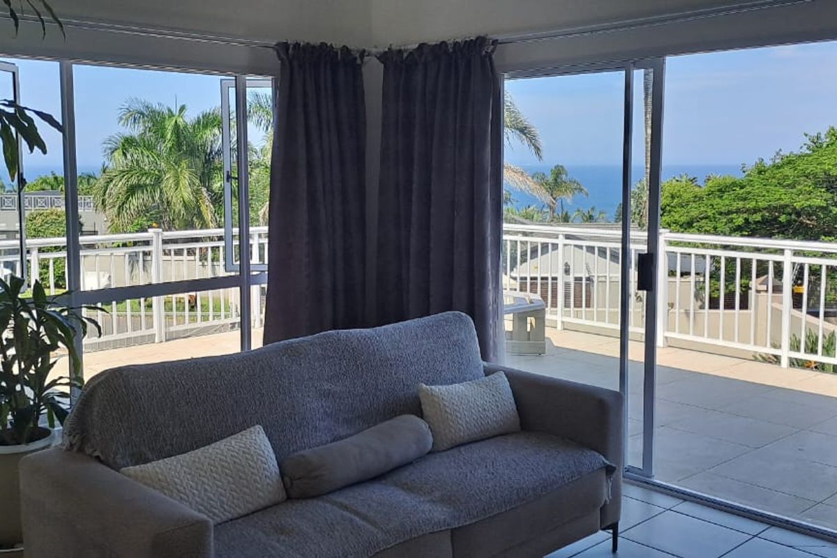 Bright living area featuring large sliding glass doors that open onto a spacious balcony with scenic coastal views.