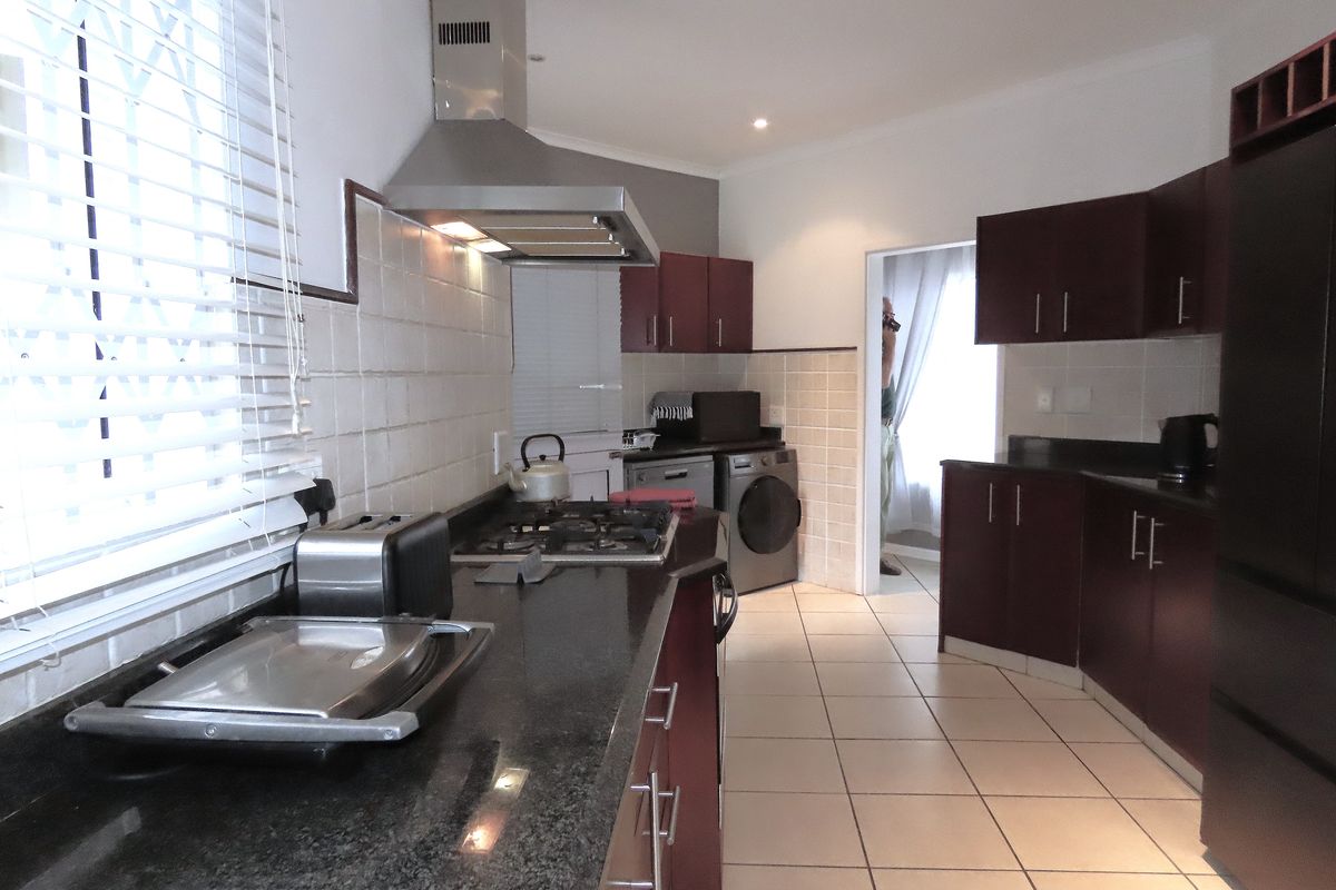 A functional kitchen featuring dark wood cabinetry, granite countertops, a gas hob with extractor fan, and tiled flooring.
