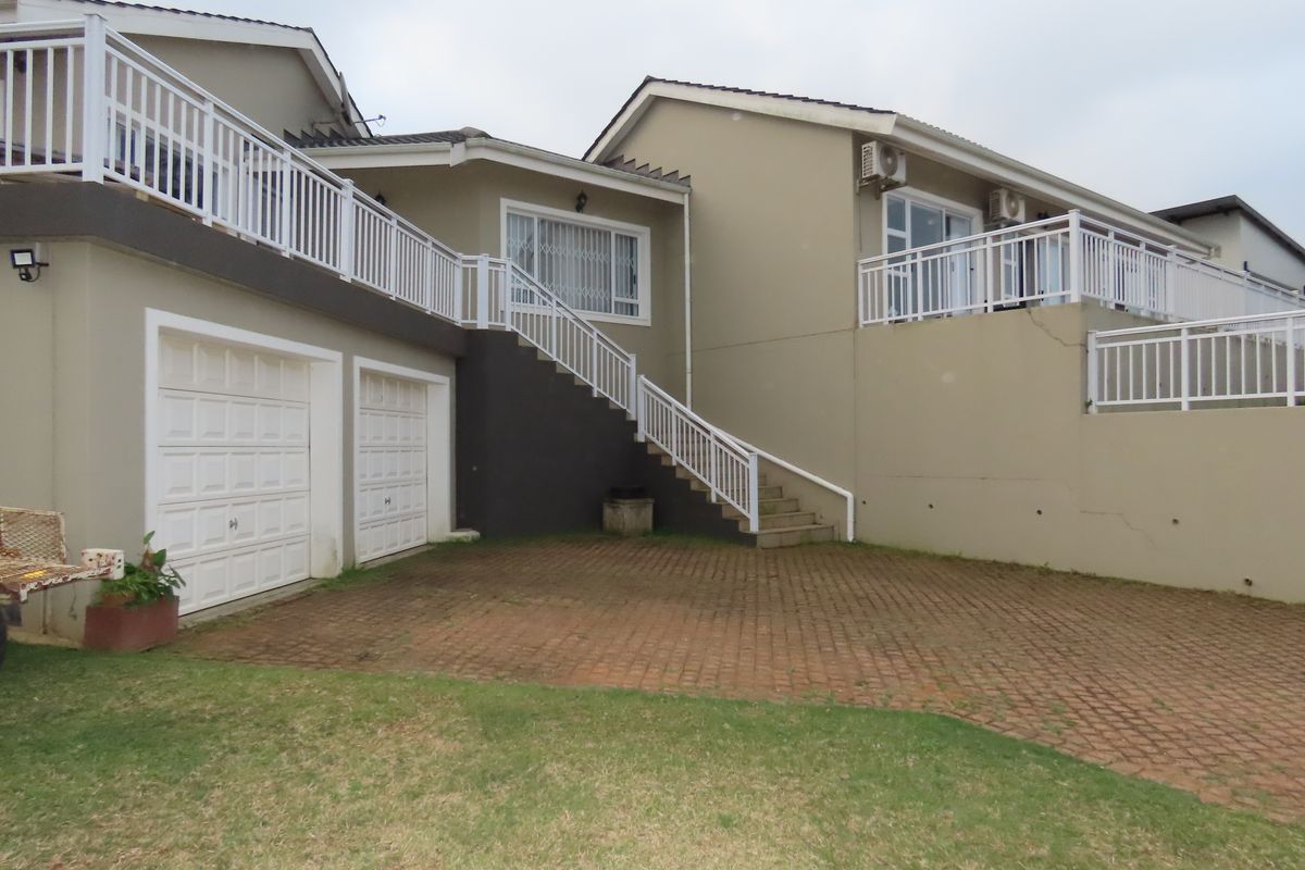 Rear exterior view showing a paved driveway, double garage, and an external staircase leading to an elevated balcony area.