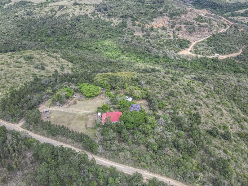 Aerial view of a small holding property featuring a dwelling with a red metal roof, surrounded by natural vegetation and accessible via a dirt road.
