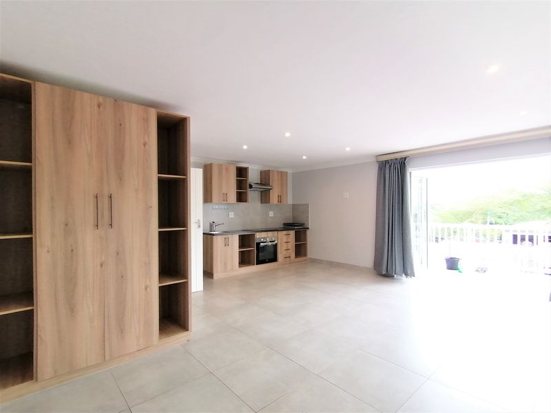 Spacious open-plan living area featuring a modern kitchen with light wood cabinetry, built-in appliances, and large sliding doors leading to a balcony.