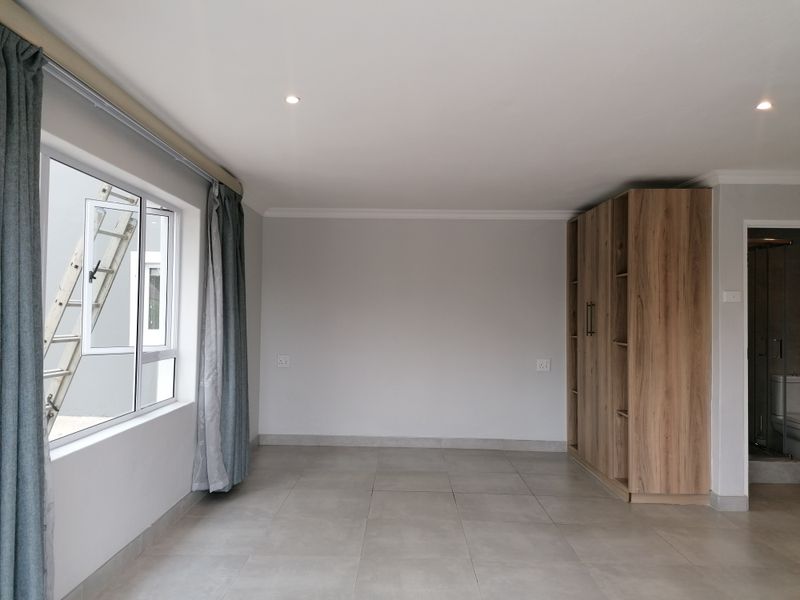 A bright, empty bedroom featuring neutral tiled flooring, recessed lighting, and a modern built-in wooden wardrobe.