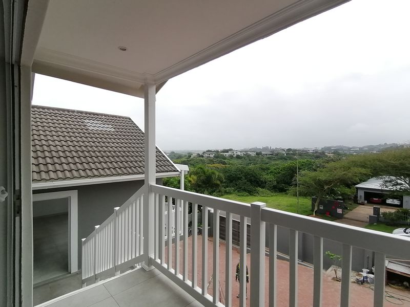 A covered balcony featuring tiled flooring and a white balustrade, offering an elevated view of the surrounding neighborhood and landscape.