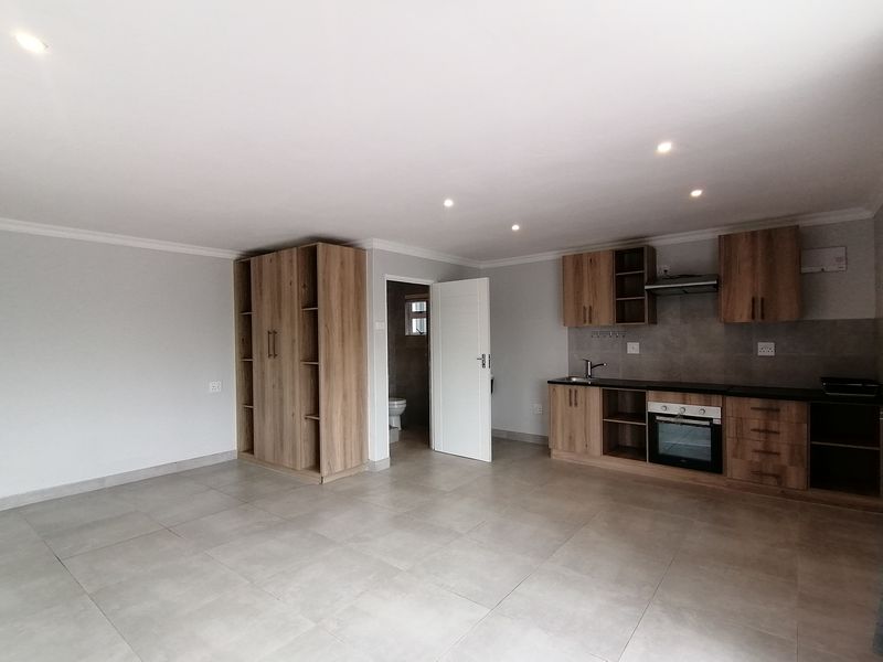 Modern open-plan living area featuring tiled floors, recessed lighting, and a contemporary kitchen with built-in cabinetry, oven, and extractor fan.