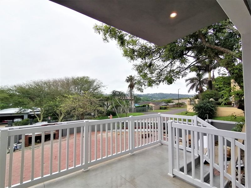 A spacious covered balcony featuring a white balustrade, tiled flooring, and a built-in brick braai, overlooking the surrounding neighborhood.