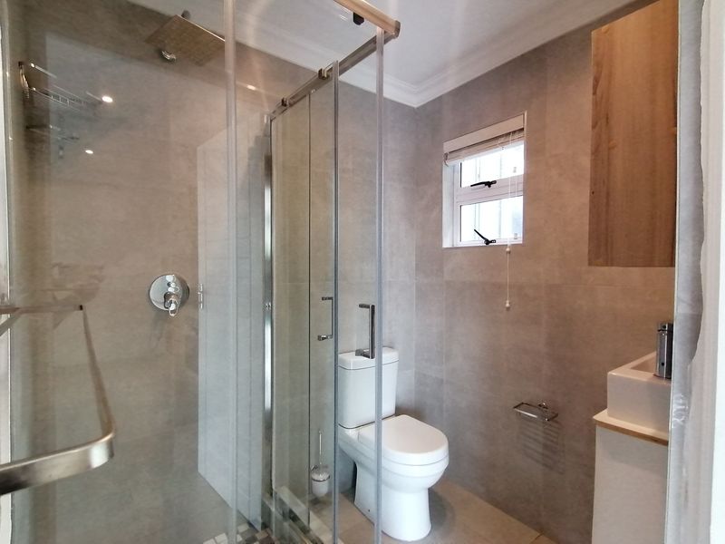Modern bathroom featuring a glass-enclosed shower with a rain shower head, a contemporary toilet, and a vanity basin with neutral wall tiling.