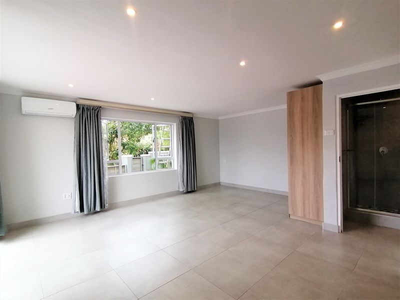 Spacious bedroom featuring neutral tiled flooring, recessed lighting, an air conditioning unit, built-in cupboard, and an en-suite shower.