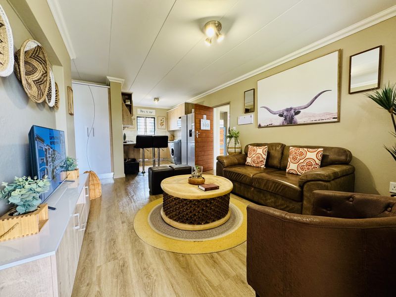 An open-plan living area featuring wood-look flooring, recessed lighting, and a compact kitchen space with built-in cabinetry and a breakfast bar.