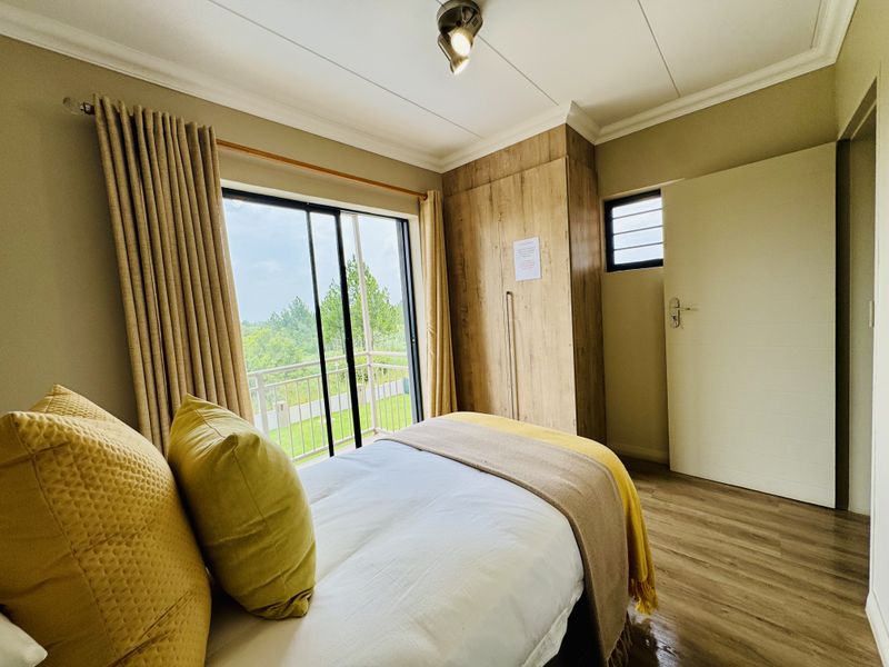 A bright bedroom featuring wood-look flooring, built-in cabinetry, and a sliding glass door that opens onto a private balcony with scenic views.
