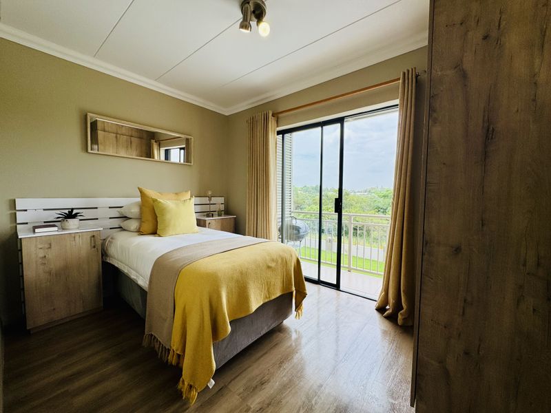 A well-maintained bedroom featuring wood-look flooring, built-in cabinetry, and sliding glass doors that open onto a private balcony with scenic views.