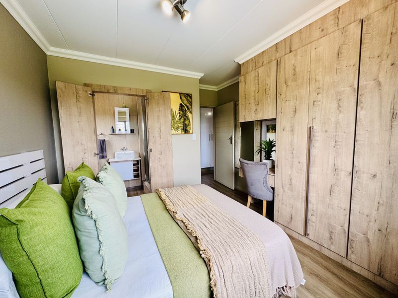 A well-appointed bedroom featuring extensive built-in wooden cabinetry, integrated vanity area, and an en-suite bathroom section with a modern basin.