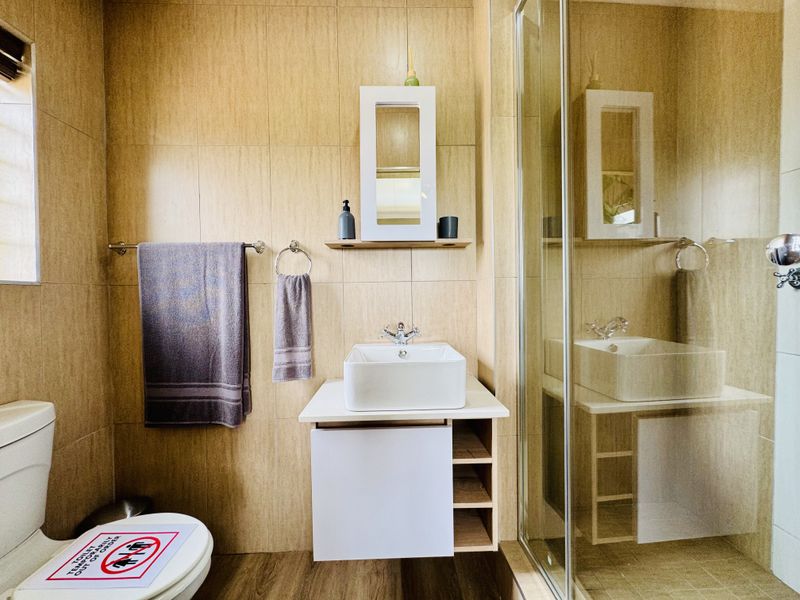 A compact bathroom featuring beige wall tiling, a modern vessel sink with a vanity cabinet, and a glass-enclosed shower area.