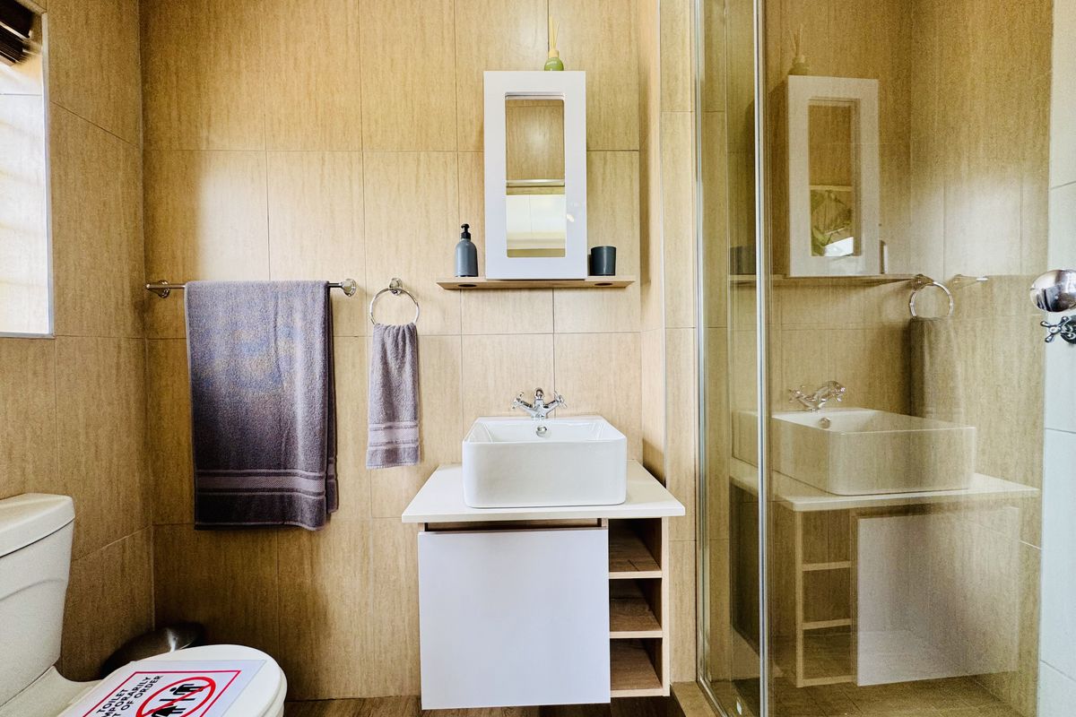 A compact bathroom featuring beige wall tiling, a modern vessel sink with a vanity cabinet, and a glass-enclosed shower area.