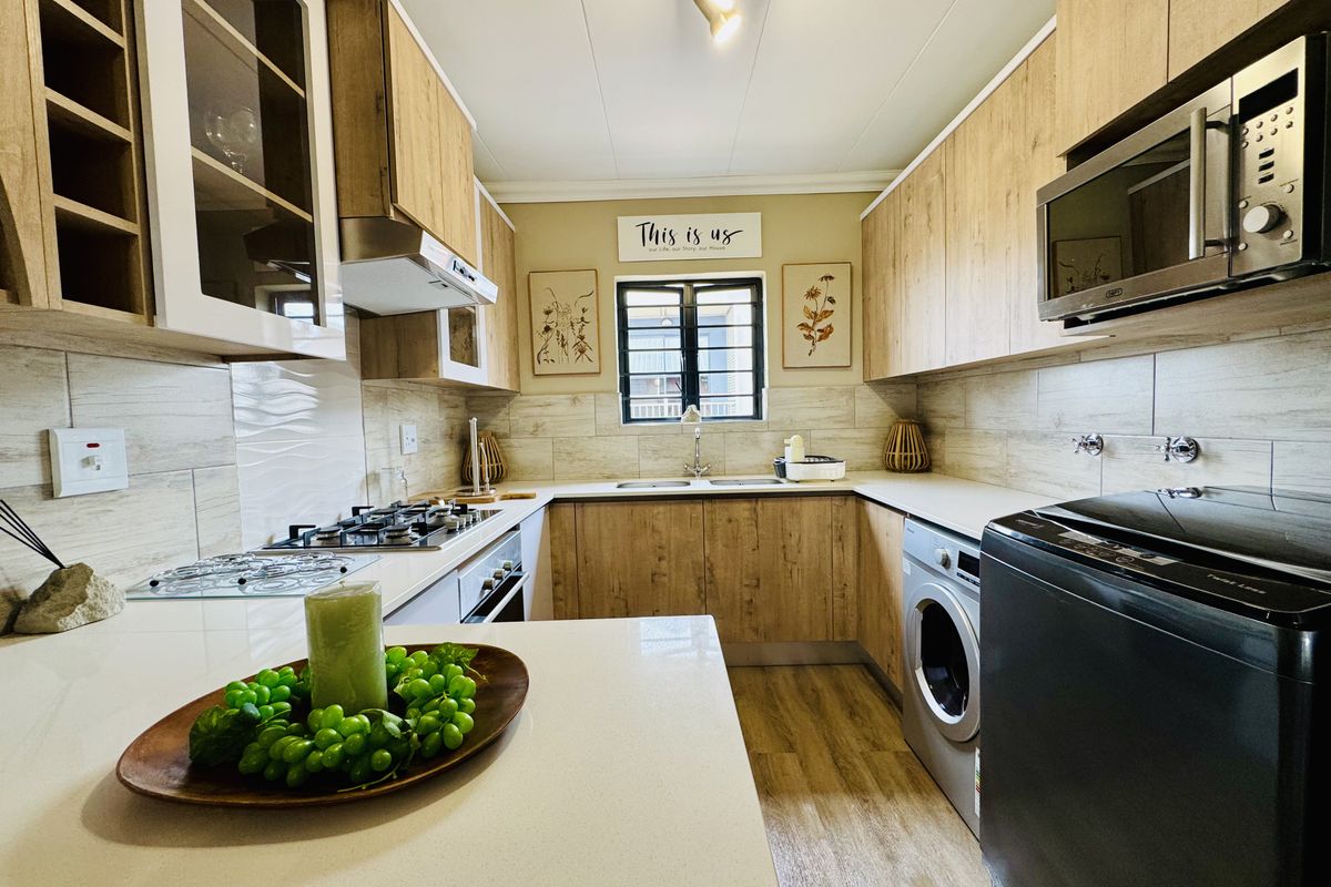 Modern galley-style kitchen featuring wood-look cabinetry, stone countertops, integrated gas hob, built-in oven, extractor fan, and space for a front-loading washing machine.
